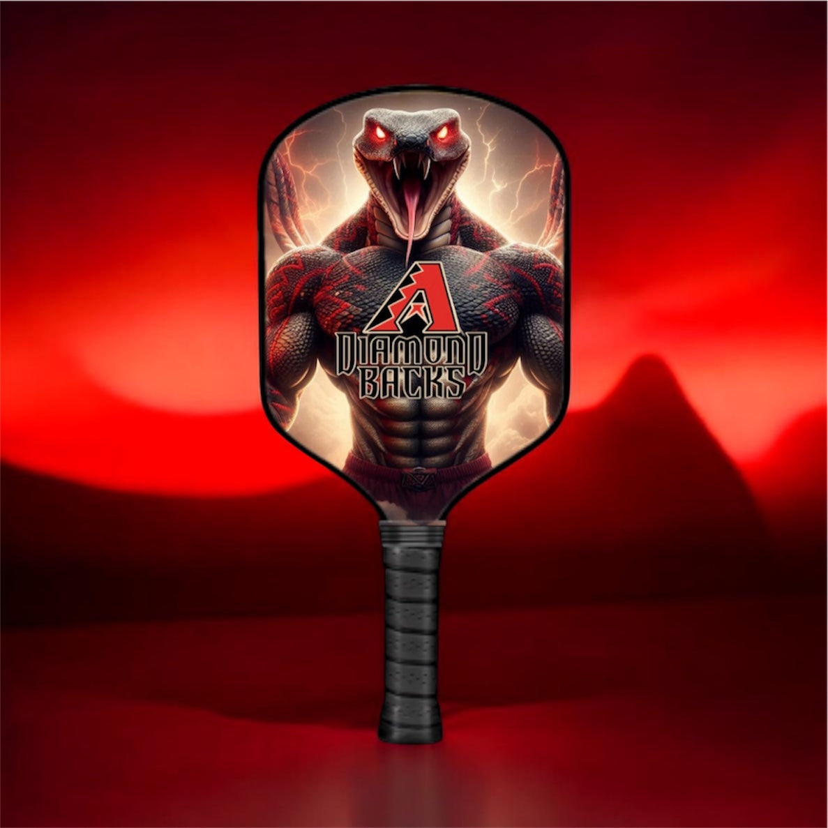 A pickleball paddle featuring a graphic of a muscular black snake with glowing red eyes and lightning, with the text 'Diamondbacks' and a red 'A' logo. The paddle has a black wrapped handle and is set against a dark red background with a mountain silhouette.