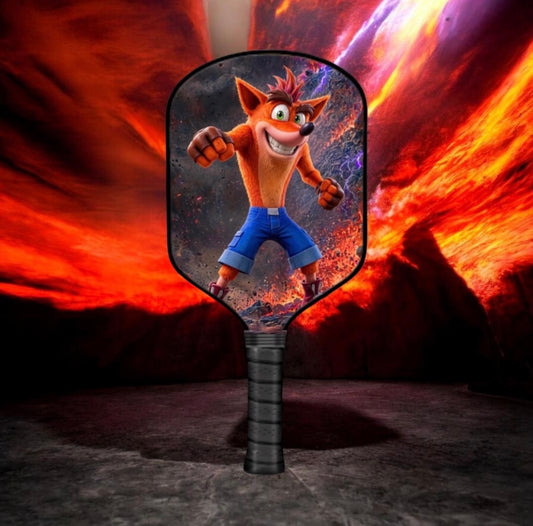 A paddle-shaped fan or mirror featuring a printed image of Crash Bandicoot, set against a dramatic fiery red and orange background.