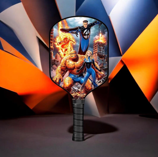 A paddled paddle-shaped fan or fan-shaped paddle with a black handle, featuring a colorful printed graphic of Marvel superheroes including the Thing, Human Torch, and Invisible Woman on the face, set against a dark abstract geometric background.