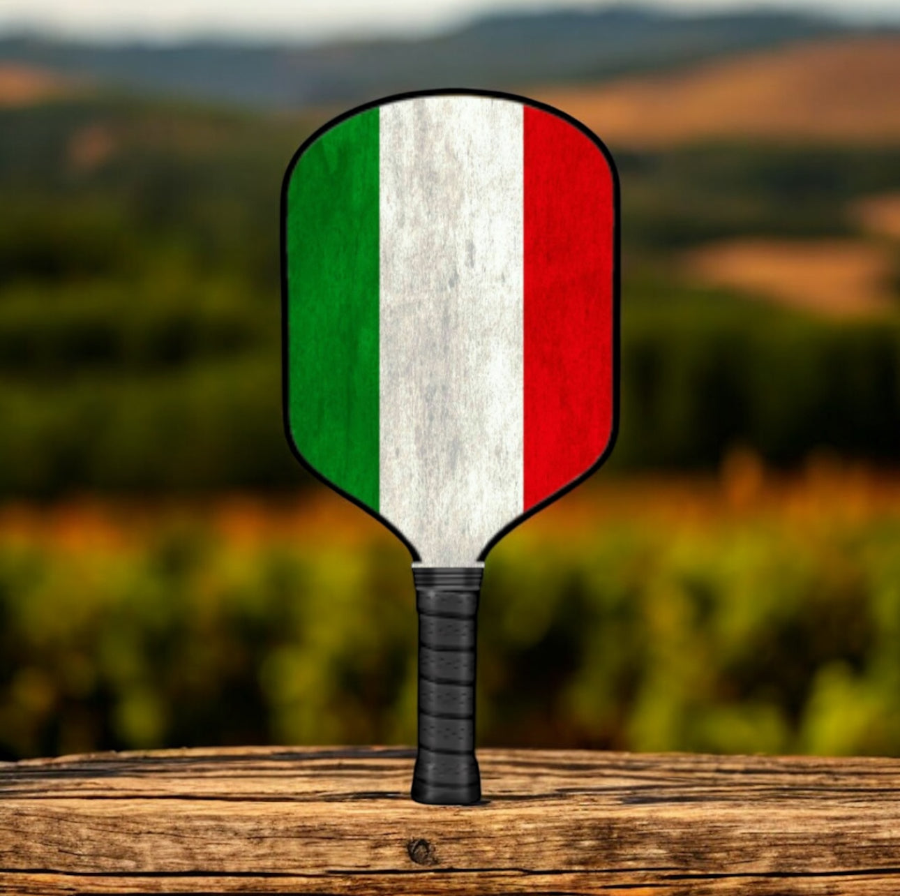 Pickleball paddle with Italian flag design on a wooden surface with a blurred natural background