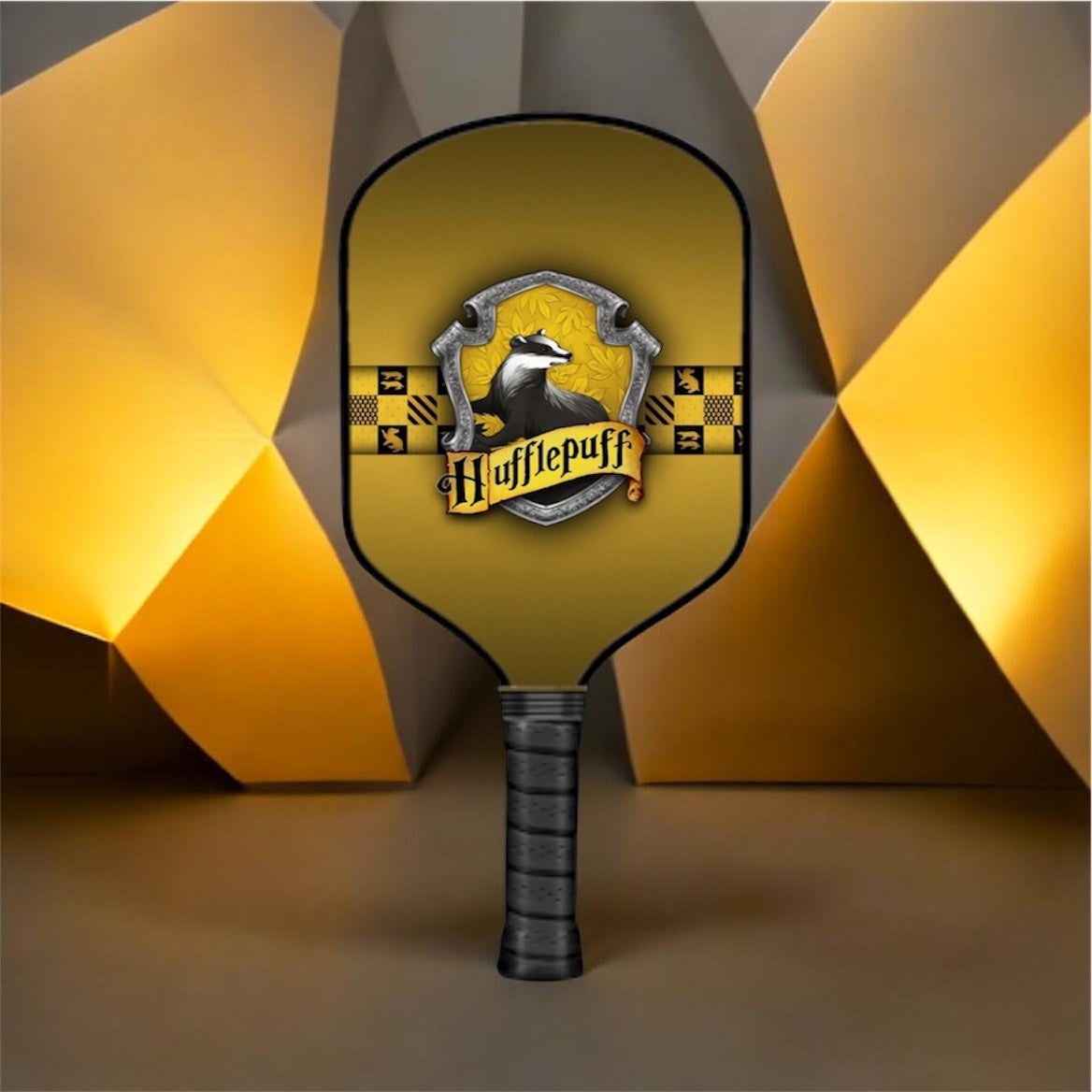 A paddle-shaped fan or light with a black handle and a gold-yellow face, featuring a shield emblem with a wolf and the text 'Hufflepuff'. The background is a stylized geometric studio setup with warm yellow and gray panels.