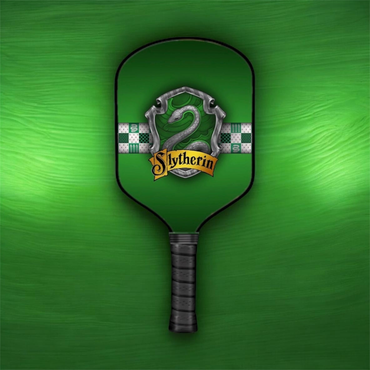 A green pickleball paddle featuring a Slytherin crest design with a silver snake, green and white checkered stripes, and a gold banner reading 'Slytherin', set against a textured green background.