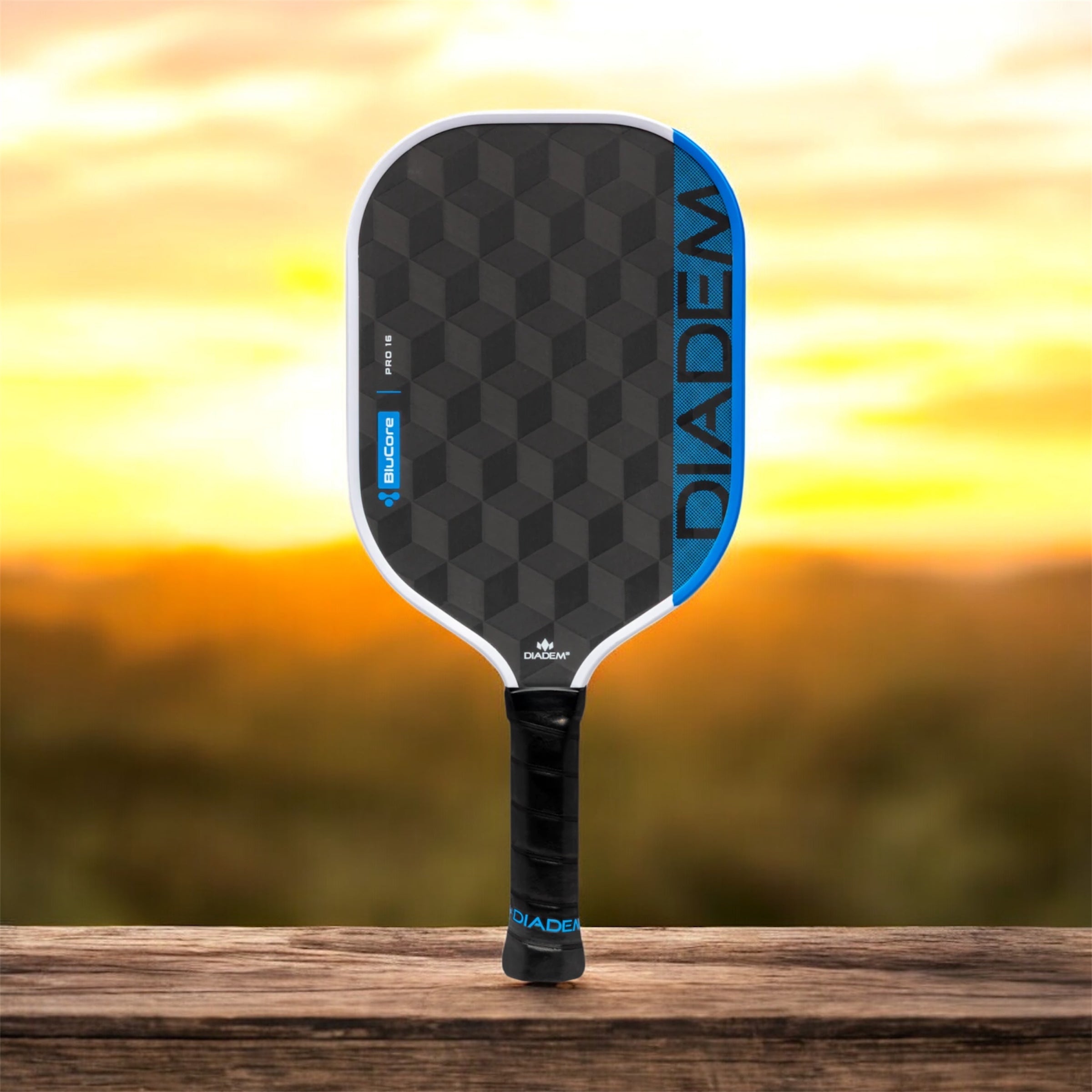 Pickleball paddle with DIADEMA branding on a wooden surface with a sunset background