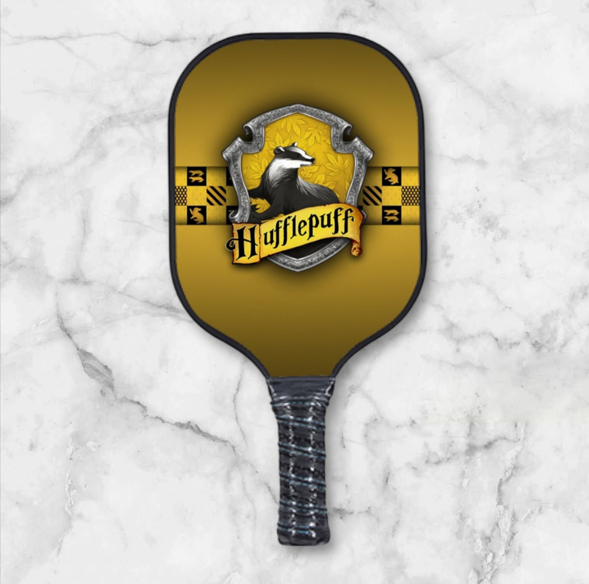 Pickleball paddle with Hufflepuff crest on a marble background