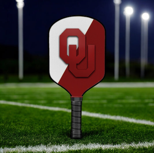 Red and white pickleball paddle withOU logo on a sports field at night