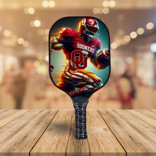 Pickleball paddle with a football player design featuring 'Sooners' on a wooden surface.