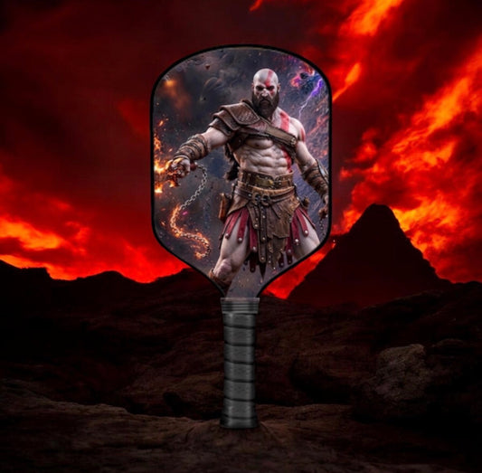 A handheld paddle-style fan or mirror with a printed Kratos character design, standing upright in a rocky outdoor scene with a dramatic red-orange sky and mountains behind it.