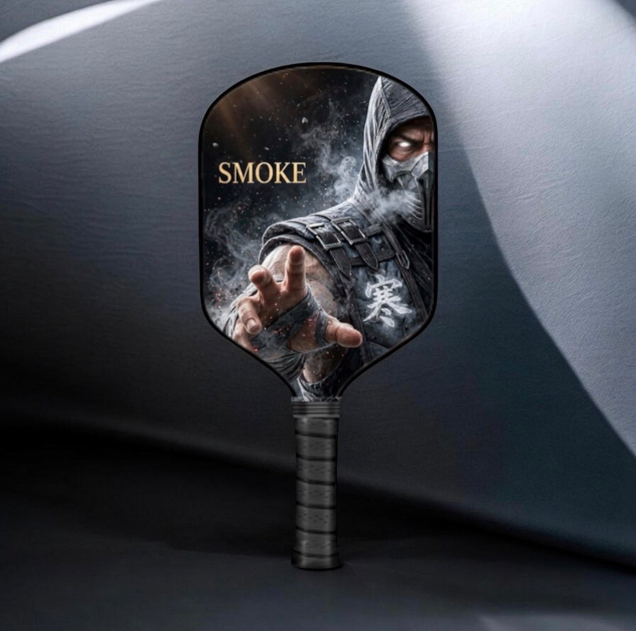 A pickleball paddle featuring a printed graphic of the character Smoke from Mortal Kombat, with his name in gold text, set against a dark gray background.