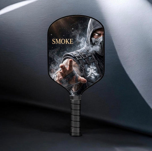 A pickleball paddle featuring a printed graphic of the character Smoke from Mortal Kombat, with his name in gold text, set against a dark gray background.