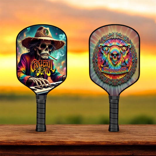 Two colorful pickleball paddles with Grateful Dead designs on a wooden surface with a sunset background.
