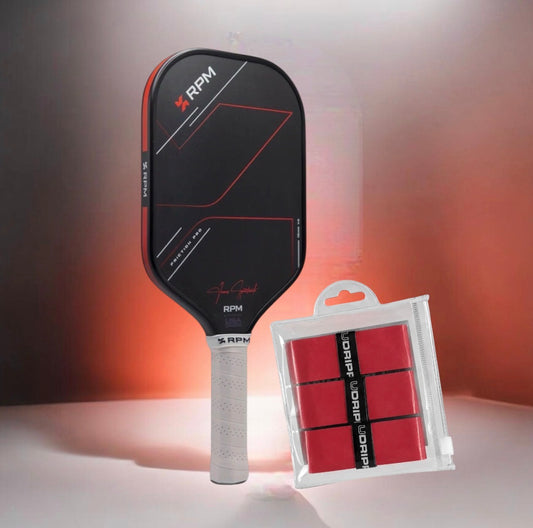An RPM pickleball paddle with a black and red face, a white wrapped handle, and a packaged set of red grip tape placed beside it on a studio surface with a warm gradient background.