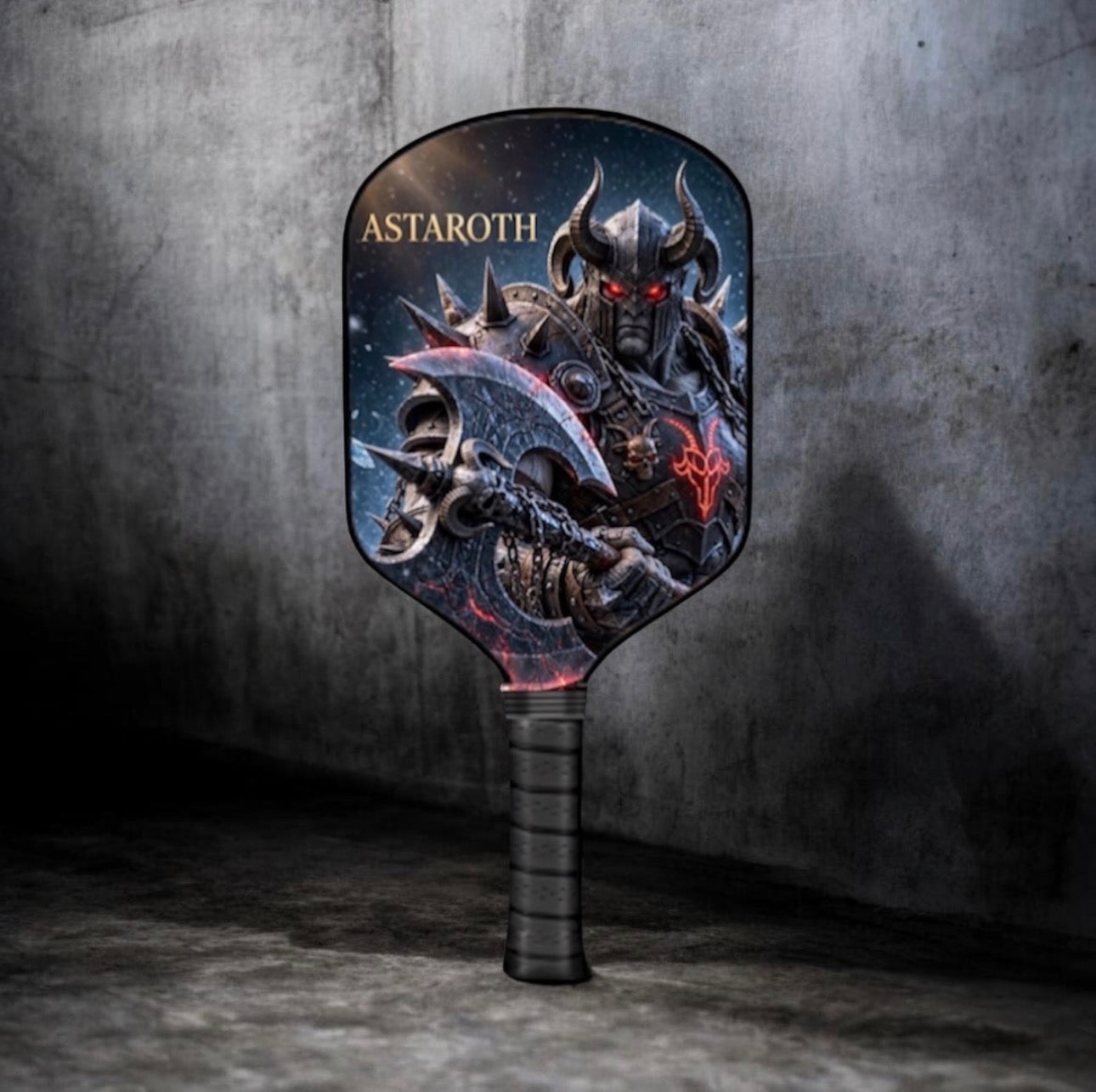 A pickleball paddle featuring a detailed graphic of a dark fantasy warrior with the name 'ASTAROTH' printed on the paddle, set against a dark, textured concrete background.
