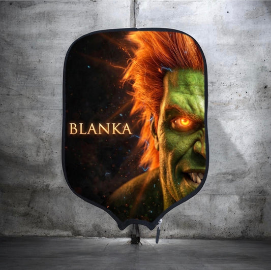 A shield-shaped fabric backdrop featuring a dramatic green monster face with glowing orange eyes and the name 'BLANKA' in gold text, displayed against a concrete wall.