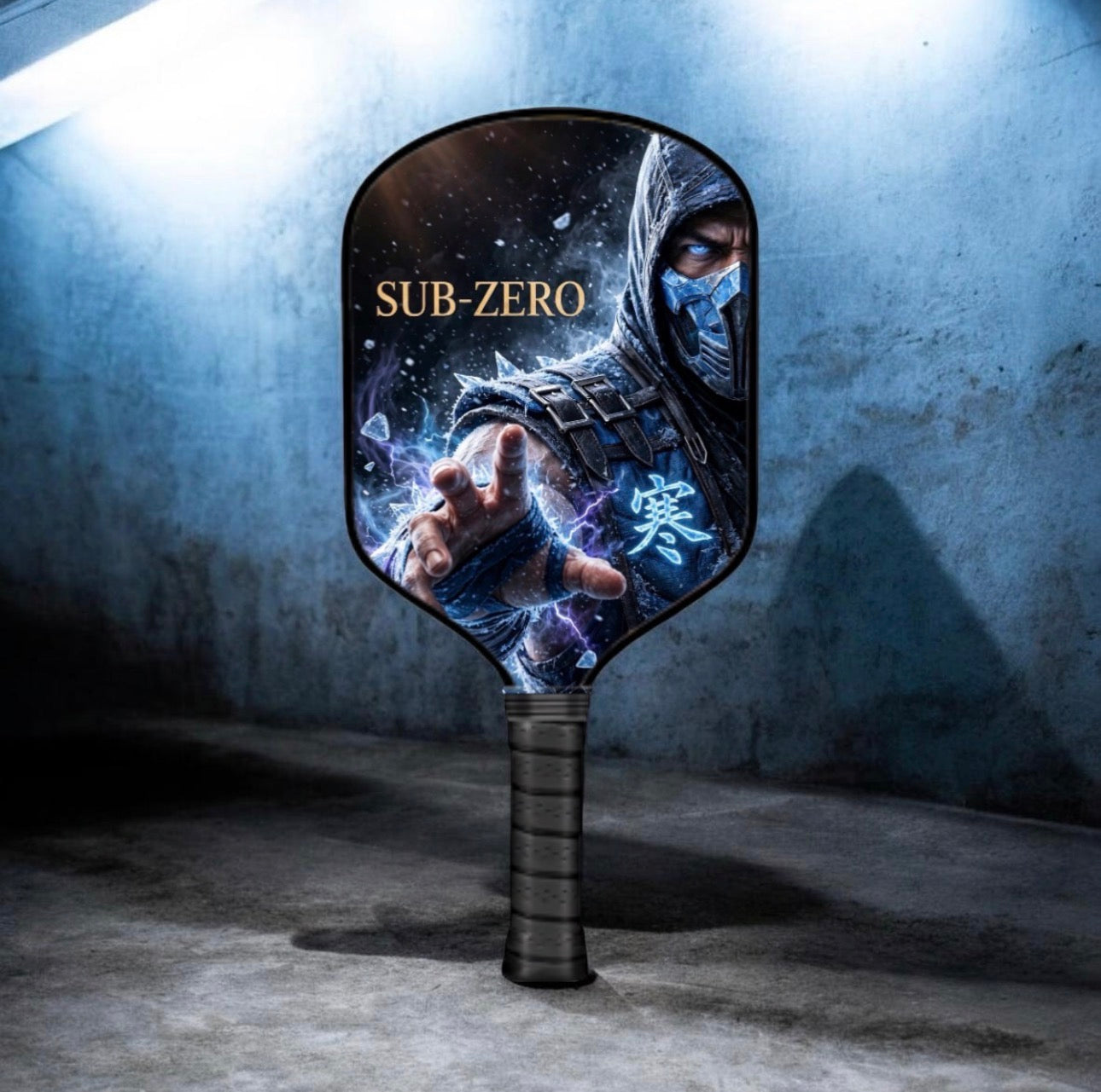 A paddle-shaped fan featuring a printed graphic of the character Sub-Zero from Mortal Kombat, standing upright against a dark, textured concrete wall.