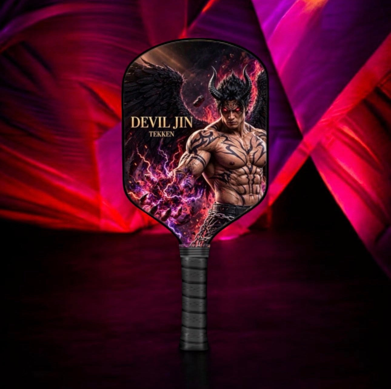 A pickleball paddle featuring a custom graphic of a muscular man with horns and wings, labeled 'DEVIL JIN TEKKEN'. The paddle has a black wrapped handle and is set against a dark background with dramatic purple and red light streaks.