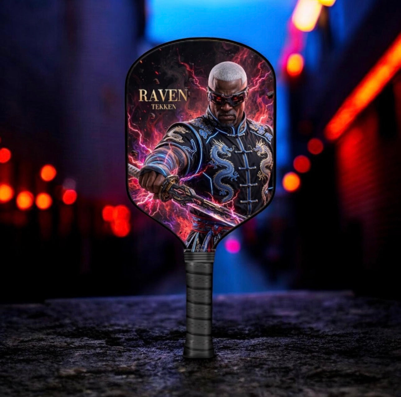 A handheld fan with a detailed graphic of a bald man in armor holding a sword, surrounded by purple and pink lightning effects, with the text 'RAVEN TEAKEN' on the blade. The fan is standing upright on a dark stone surface with a blurred, colorful alleyway background.