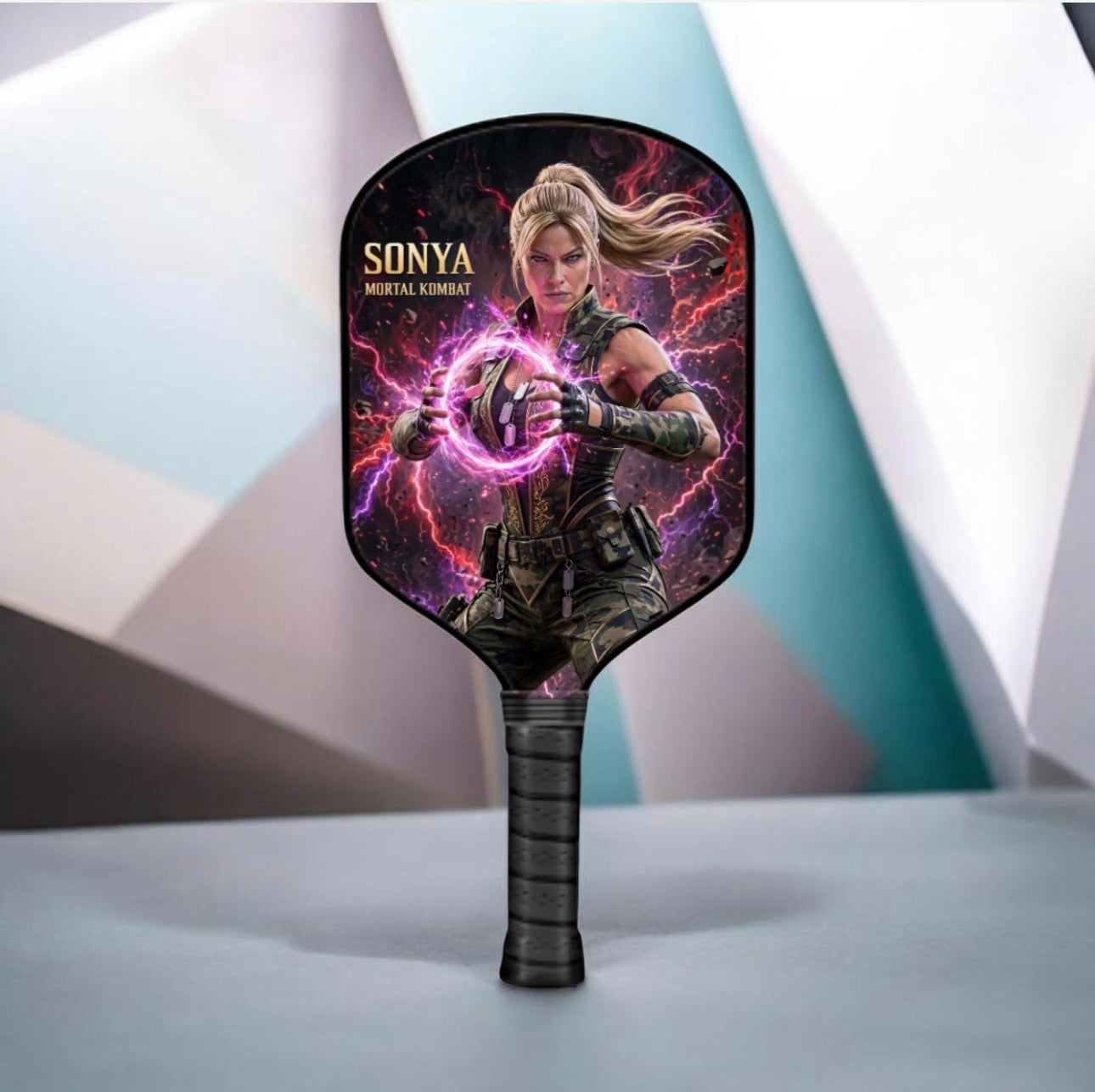 A handheld paddle fan featuring a printed graphic of Sonya from Mortal Kombat, with her name and character title printed on the face of the paddle. The fan has a black handle with a black grip.